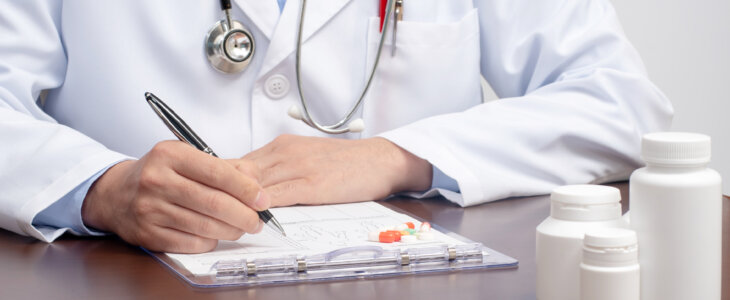 A male doctor writing on the medical form with the stethoscope nearby